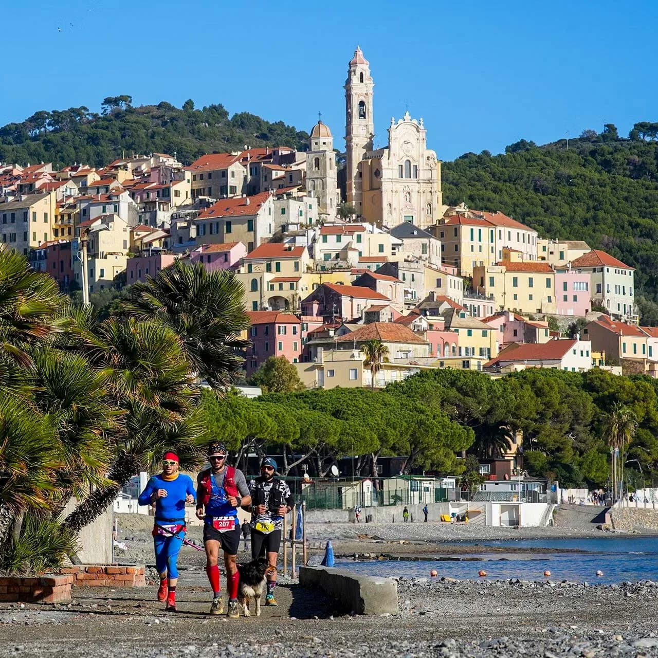 Atleti e cani sulla spiaggia sotto il borgo di Cervo